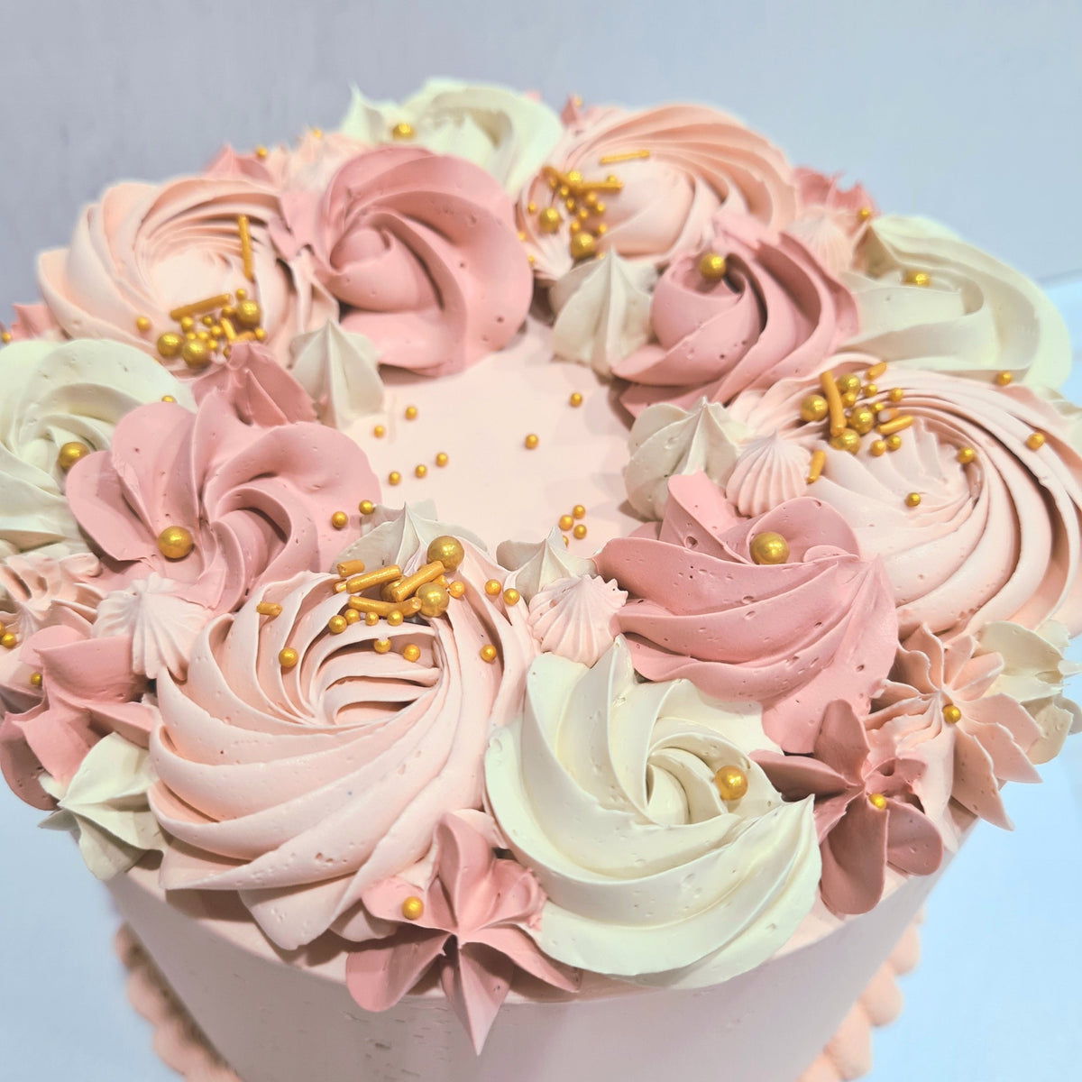 Decorative cake with pink, white, and gold frosting on a light blue background