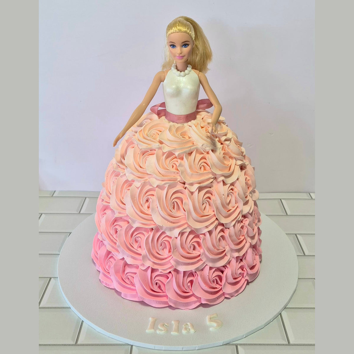 Barbie doll cake with a pink and orange ombre dress on a white background