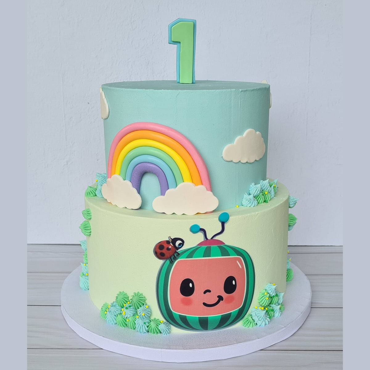 Children's birthday cake with a cartoon character, rainbow, and clouds on a light blue background.