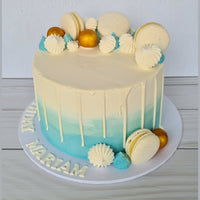 Decorative cake with white and blue gradient, macarons, and spherical decorations on a light gray background.