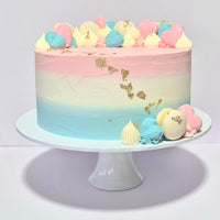 Pastel-colored cake with decorative elements on a white stand against a light gray background