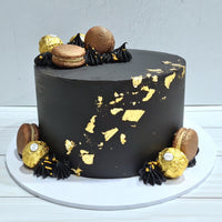 Black cake with gold leaf decorations on a white surface