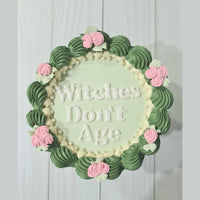 Decorative wall art with 'Witches Don't Age' text and floral design on a light background