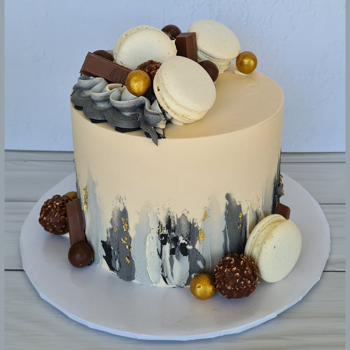 Decorative cake with macarons and chocolate on a white plate against a light blue background