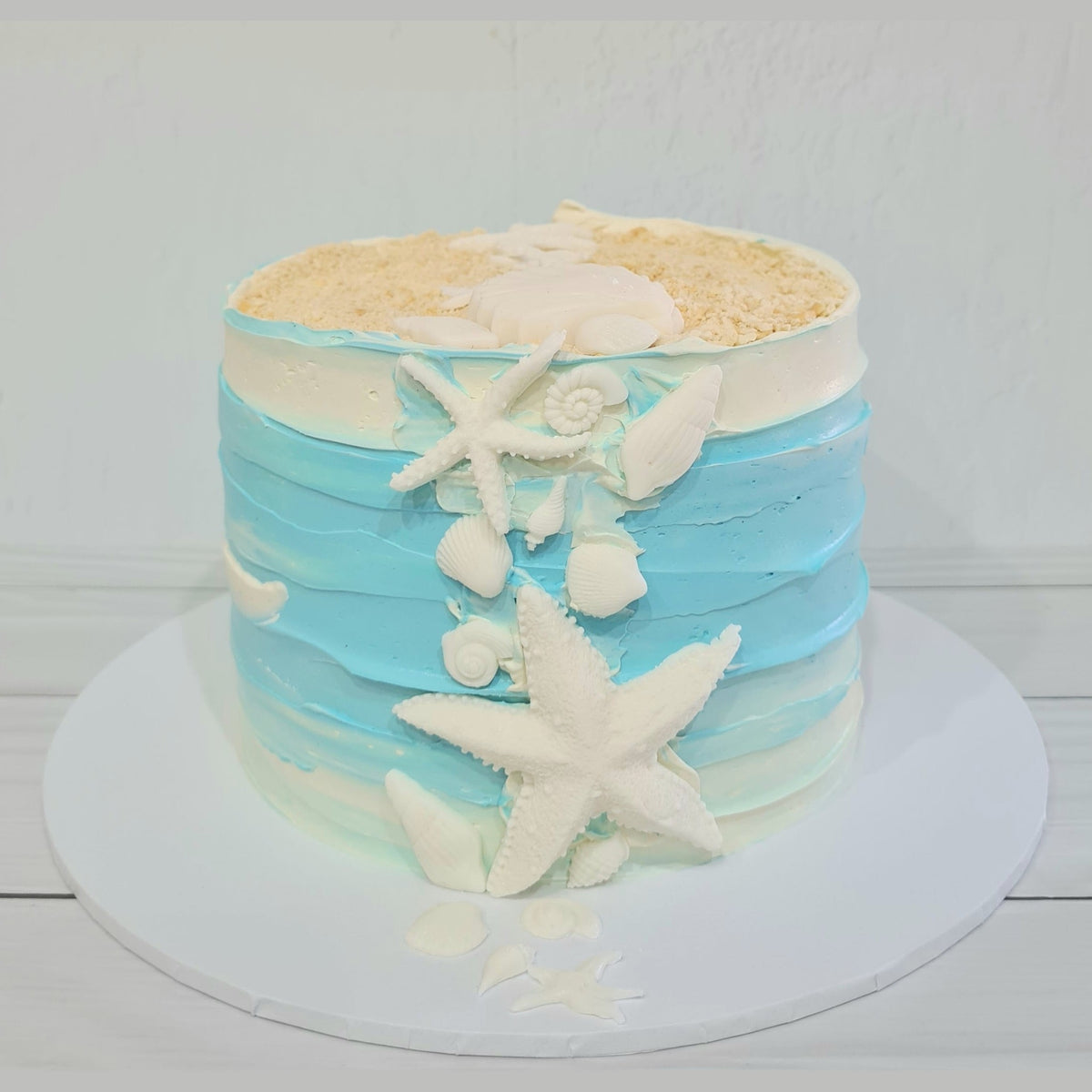 Cake with blue and white frosting, starfish, and shells on a white background