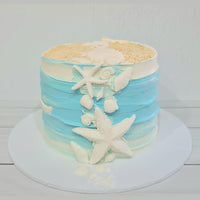 Cake with blue and white frosting, starfish, and shells on a white background
