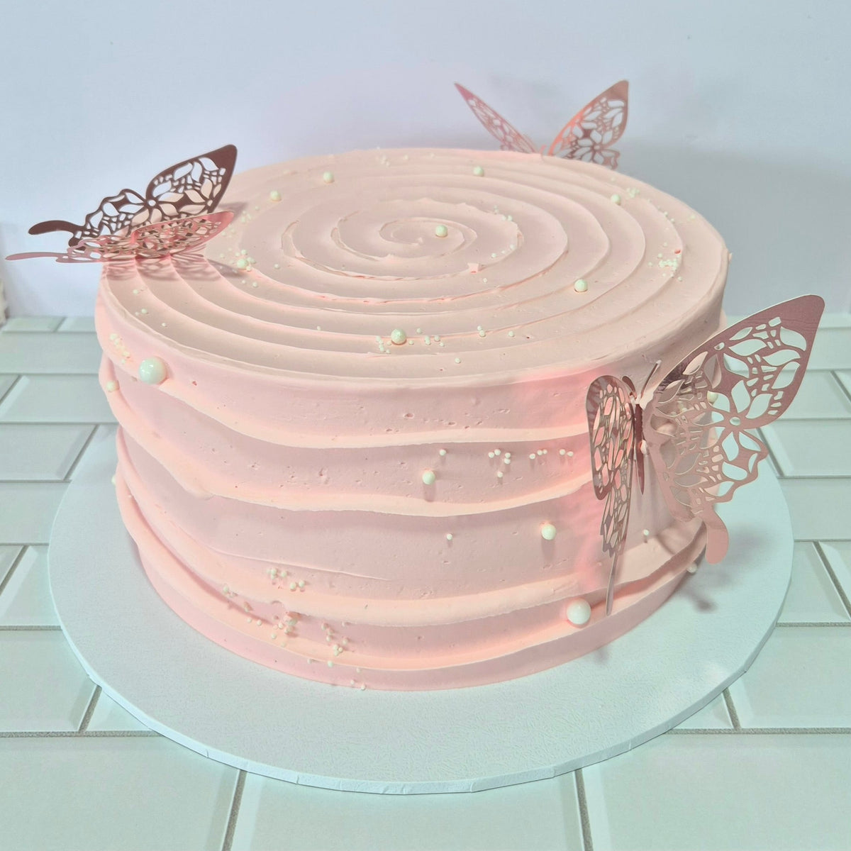 Pink cake with butterfly decorations on a white tiled floor