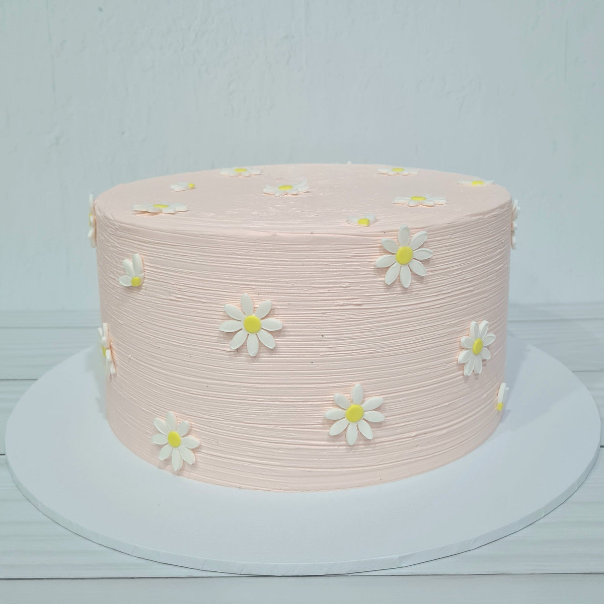 Pink cake with white daisy flowers on a light gray background