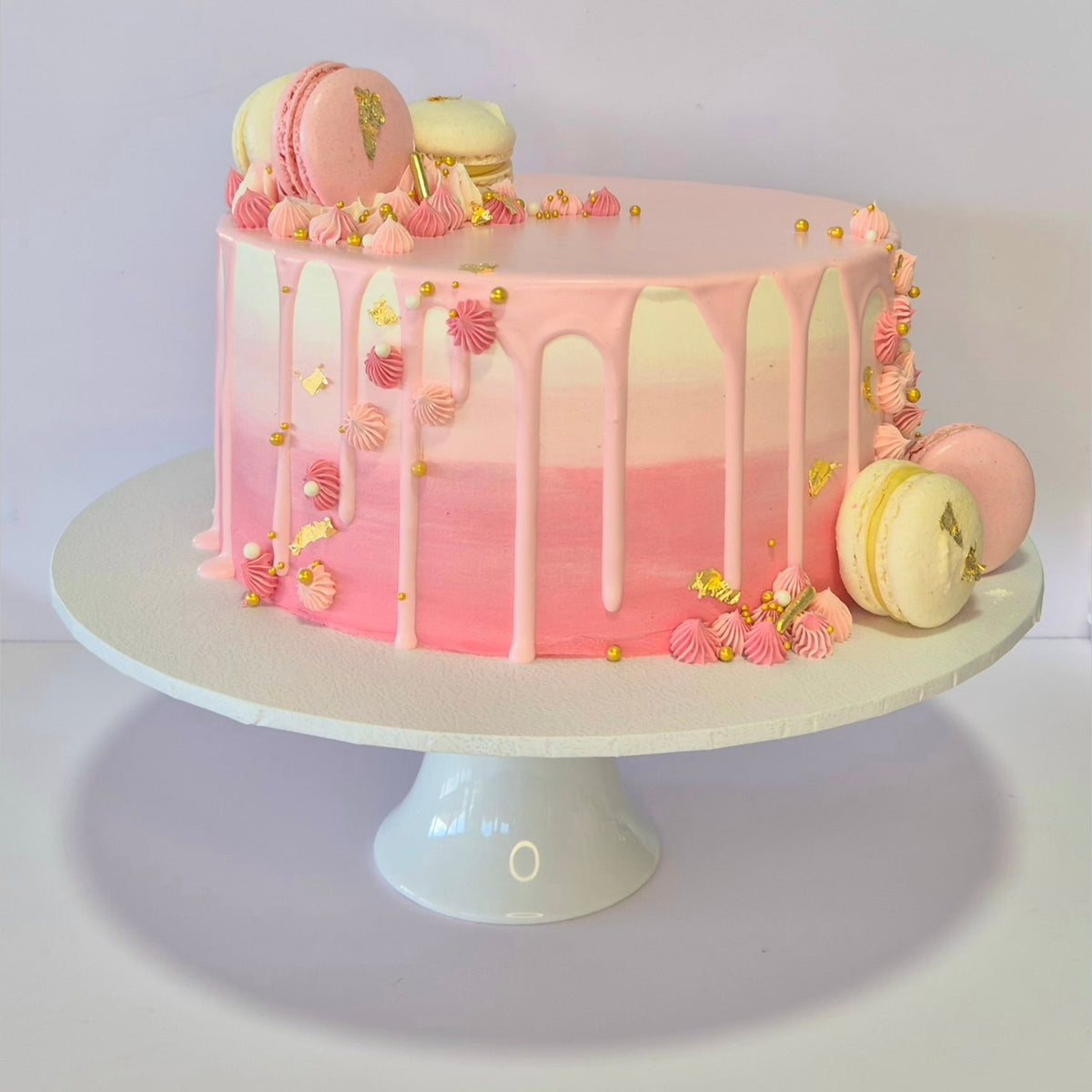 Pink and white cake with macarons on a white stand against a light gray background