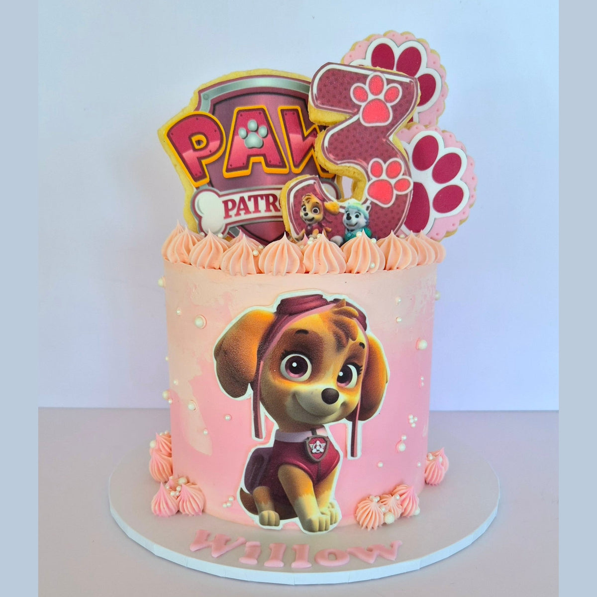 Pink cake with Paw Patrol theme featuring cartoon characters and decorations.