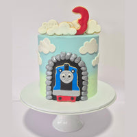 Children's birthday cake with Thomas the Tank Engine design on a white stand.