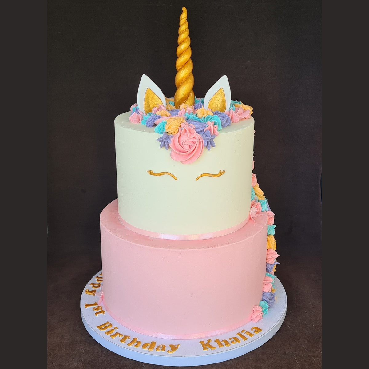 Two-tiered unicorn-themed birthday cake with colorful decorations on a dark background