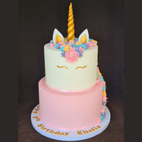 Two-tiered unicorn-themed birthday cake with colorful decorations on a dark background