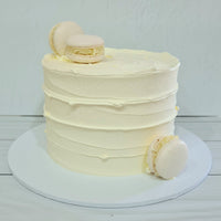 White frosted cake with macarons on a white background
